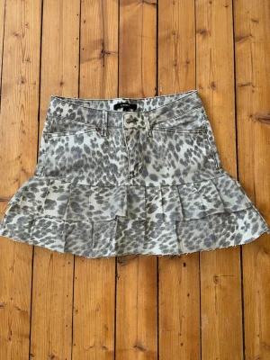 Leopardmönstrad volangkjol  - Cool kort kjol, märke Lindex, med leopardmönster i grå och beige toner. Kjolen har volang nertill, klassisk jeansmodell med fickor fram och bak. Perfekt för dig som vill sticka ut med en trendig look. Noggrant sydd kjol.