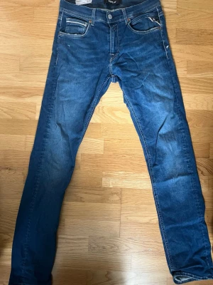 Blå raka jeans från Replay - Säljer ett par klassiska blå jeans från Replay, modell Grover. Jeansen har rak passform, fem fickor och snygga kontrastsömmar. Tillverkade i slitstarkt denim med en lätt tvättad look. Perfekta för dig som gillar en tidlös och enkel stil.
