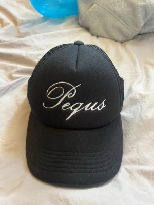 Svart keps från Pequs med mesh - Svart keps från Pequs med vit broderad logga framtill och mesh på baksidan för extra ventilation. Justerbar snapback-stängning gör att den passar de flesta. Perfekt för en avslappnad och trendig stil.