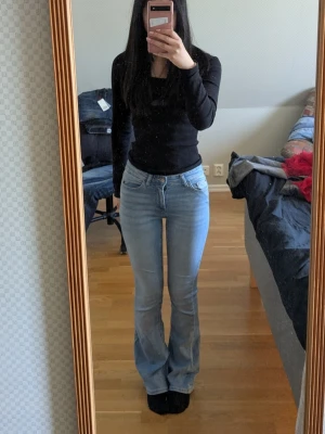 Ljusblå bootcut jeans från ONLY - Säljer ett par ljusblå bootcut jeans från ONLY med klassisk femficksdesign och normal midja. Jeansen har en snygg tvätt och är tillverkade i mjukt denimtyg som sitter bekvämt. Perfekta för dig som gillar en avslappnad men trendig look.