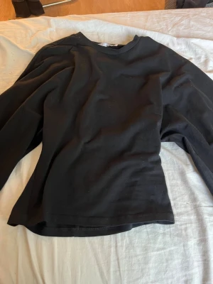 Svart långärmad topp i bomull - En enkel svart långärmad topp med rund halsringning. Tillverkad i mjuk bomull som känns skön mot huden. Perfekt att styla med jeans eller kjol för en clean och stilren look.Den är tight i midjan och utsvängd i armarna 