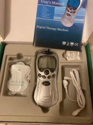 Digital Therapy Machine med tillbehör - Digital Therapy Machine i silverfärg med LCD-skärm, flera knappar och tillhörande elektrodpads, sladd och användarmanual. Perfekt för elektronisk muskelstimulering och avslappning. Kommer i originalförpackning.