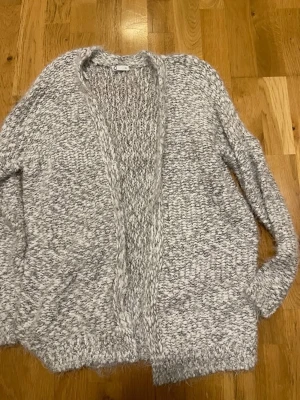 Gråmelerad stickad kofta från Cubus stl S  - Mysig och oversized gråmelerad stickad kofta från C&A. Koftan har öppen front utan knappar, lång ärm och grovstickat material som känns riktigt fluffigt. Perfekt för lager-på-lager och chill dagar.