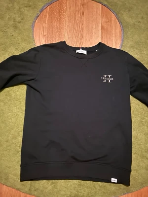 Svart sweatshirt från Les Deux - Stilren svart sweatshirt från Les Deux med diskret logga på bröstet. Tröjan har rund halsringning och långa ärmar, perfekt för en avslappnad och trendig look.