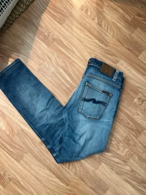 Blå jeans från Nudie Jeans - Säljer ett par klassiska blå jeans från Nudie Jeans med snygg slitning och raka ben.  Den klassiska brodyren på bakfickorna. Grim trim W30 L32
