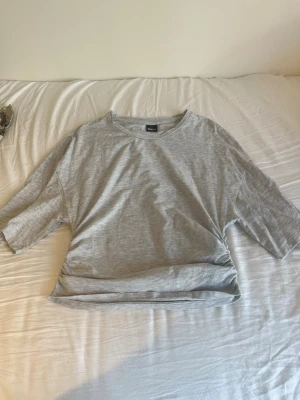 Grå basic t-shirt från Gina Tricot  - En enkel och stilren grå t-shirt från Gina Tricot, den är loose vid armarna men tight runt midjan. Perfekt för en fin vårdag. Tröjan är i storlek L, men är liten i storleken så jag tycker att den sitter som en S/M.