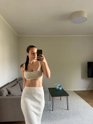 Ribbat vitt set med topp och kjol - Säljer ett ribbat set i vitt med en croppad topp med breda axelband och en matchande lång kjol med hög midja. Setet är i mjukt, stretchigt material och har en stilren, enkel design. Perfekt för en trendig och avslappnad look. Topp: L. Kjol: M