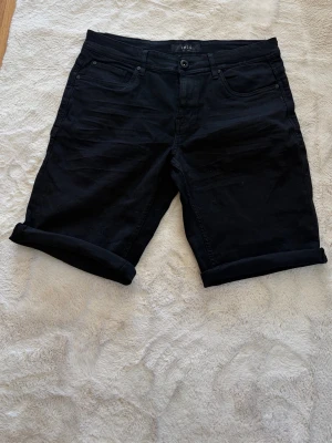 Svarta shorts , storlek M - Svarta shorts  i klassisk femficksmodell. De har upprullade benslut och stängs med knapp och dragkedja. Perfekta för sommaren och lätta att matcha med olika outfits. Materialet är mjukt och bekvämt, troligtvis bomull med lite stretch.