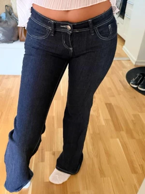 Mörkblå bootcut jeans med låg midja -  Snygga mörkblå bootcut jeans med låg midja och vita kontrastsömmar. Klassisk femficksmodell i stretchigt denimtyg som sitter tajt upptill och släpper ut vid benen. Perfekta för en trendig och avslappnad look.