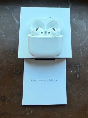 Apple AirPods med laddningsetui - Säljer ett par vita Apple AirPods med trådlöst laddningsetui. Snygg och stilren design i blank plast, perfekt för dig som vill ha smidiga hörlurar till mobilen. Kommer i originalförpackning med tillhörande tillbehör. Helt nya i förpackning. 