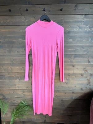Rosa ribbad långärmad klänning - Trendig rosa långklänning med ribbad struktur och lång ärm. Klänningen har en hög hals och är figurnära i modellen, perfekt för dig som gillar en enkel men snygg look. Materialet känns mjukt och stretchigt, vilket gör den bekväm att bära. Passar small/medium pga stretchigheten. 