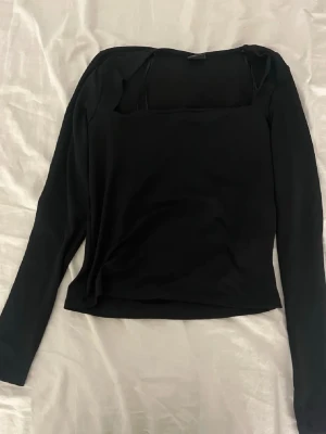 Svart långärmad topp från Gina Tricot - Svart långärmad topp från Gina Tricot med fyrkantig ringning. Toppens material känns mjukt och stretchigt, perfekt för en stilren look. Passformen är normal och modellen är enkel utan mönster eller extra detaljer.