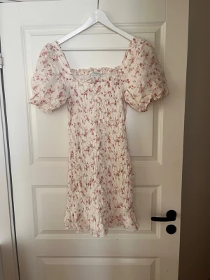 Såå fin klänning  från Neo Noir - Supersöt klänning från Neo Noir  med rosa blommigt mönster. Puffärmar och smokad/ krinklat material med volangkant nedtill. Perfekt för sommarens alla tillfällen och ger en romantisk vibe 🥰