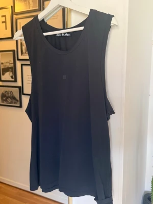 Svart ärmlös linnetopp Acne Studios - Minimalistisk svart linnetopp från Acne Studios med rund halsringning och breda axelband. Toppen är ärmlös och har en loose passform, perfekt för en clean och avslappnad stil. Materialet känns mjukt och svalt mot huden. OBS !Det finns en hål framme ( vet ej varifrån har kommit) ca 1 mm försökte att ta bild på den men det gick inte pga är väldigt liten och syns inte på bild . Annas är nästan nytt 