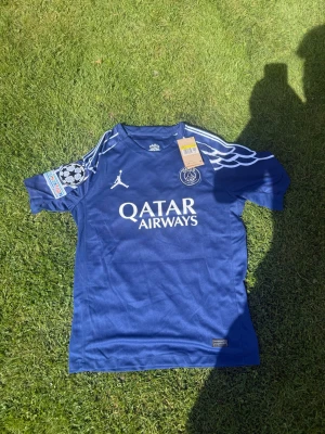 Blå PSG matchtröja Zaire-Emery #33 - Snygg blå PSG matchtröja med vita detaljer, Qatar Airways-tryck och Champions League-märke på ärmen. Zaire-Emery och nummer 33 på ryggen. Tillverkad i lätt och ventilerande material, perfekt för fotboll eller träning. Helt ny, Pris kan diskuteras 