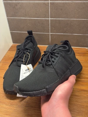 HELT NYA- Svarta Adidas NMD_R1 primeblue sneakers  - Helt nya Adidas NMD_R1 Primeblue svarta.  Aldrig använda, lappen sitter kvar.  Storlek 37 1/3    Säljer då de inte kom till användning   Pris kan diskuteras vid snabb affär