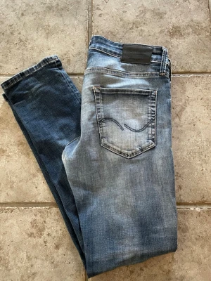 Blå jeans från Jack & Jones - Snygga blå slim fit jeans från Jack & Jones  med slitningar på låren och knäna. Jeansen har klassisk femficksdesign, ljus tvätt framtill och mörkare partier på benen. Perfekta för en avslappnad och trendig look.