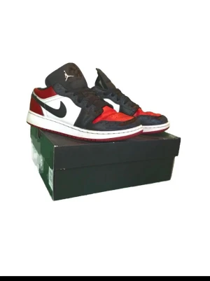 Air Jordan 1 Low Bred Black/Red/White - Snygga Air Jordan 1 Low sneakers i klassiska färgerna svart, rött och vitt. Skorna är köpta i november 2025. säljer med anledning av att de inte passar längre. Den högra skon har tagit lite stryk i hälen som ses på en av bilderna, men går att fixa om man är engagerad och påhittig.Den vänstra är lite bättre. Ett av skosnören är lite upprivet men du får kontakta mig så löser vi nytt skosnöre. När jag köpte den nya från sneak kostade dem 1900. Pris kan diskuteras.