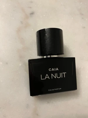 CAIA La Nuit Eau de Parfum - Snygg parfymflaska från CAIA i modellen La Nuit. ENDAST TESTAD. Flaskan är svart med stilren design och har ett matchande svart lock. Eau de Parfum-varianten ger en lyxig känsla och passar perfekt för dig som gillar eleganta dofter. 