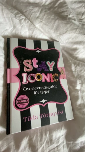 Stay Iconic: Överlevnadsguide för tjejer - En färgstark och inspirerande bok med svartvita ränder och rosa detaljer, skriven av Tilda Törnqvist. Boken är en överlevnadsguide för tjejer och bjuder på pepp, tips och motivation. Perfekt för dig som vill boosta självförtroendet och hitta din ikoniska stil.