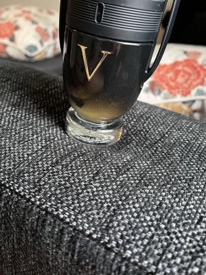 Paco Rabanne Invictus Victory parfym - Säljer en Paco Rabanne Invictus Victory parfym i en cool svart och guldfärgad flaska formad som en pokal. Flaskan har ett stort V i guld på framsidan och är tillverkad i glas och plast. Perfekt för dig som gillar exklusiva och kraftfulla dofter.