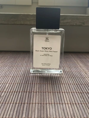 TryScent Tokyo Eau de Parfum 50 ml - Tokyo från TryScent är en eau de parfum inspirerad av Le Labo Gaiac 10 Tokyo. Doften har noter av mysk, guajac-trä och svartpeppar. Flaskan är rektangulär i genomskinligt glas med svart fyrkantigt lock och minimalistisk vit etikett.