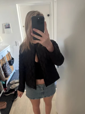Svart quiltad jacka - Svart quiltad bomberjacka med rund hals och knäppning framtill. Jackan har en kort och boxig passform som ger en cool look. Perfekt att slänga över en crop top eller hoodie. Materialet är troligtvis polyester och jackan har långa ärmar.