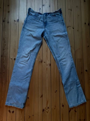 Ljusblå raka jeans i klassisk modell - Säljer ett par ljusblå jeans med rak passform och fem klassiska fickor. Jeansen har normal midja och stängs med knappar. Perfekta för en avslappnad och tidlös look.