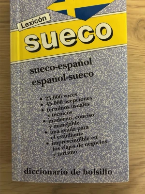Lexicón sueco-spansk fickordbok - En smidig ordbok i fickformat för svenska och spanska. Omslaget är grått med gula och blå detaljer samt svensk flagga. Innehåller 25 000 ord och 45 000 betydelser, både vanliga och tekniska termer. Perfekt för studier, resor och affärer.