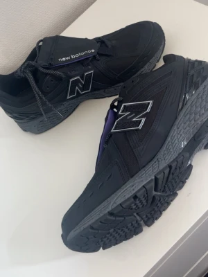 Svarta New Balance sneakers - Snygga svarta sneakers från New Balance med silverfärgad N-logga på sidan. Skorna har en chunky sula och detaljer i mesh och syntetmaterial. Perfekta för dig som gillar en sportig och modern stil.