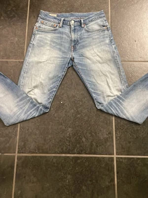 Levi's 512 ljusblå jeans - Klassiska Levi's 512 jeans i ljusblå tvätt med raka ben och femficksmodell. Jeansen har en snygg slitning framtill och bak, samt knappgylf. Perfekta för en avslappnad och trendig look. Storlek W31 L32