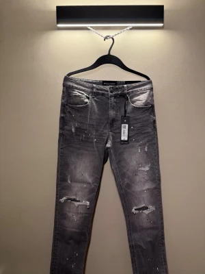 Grå slitna jeans Supply & Demand - Säljer ett par grå jeans från Supply & Demand med slitningar, färgstänk och tvättad look. Jeansen har fem fickor, normal midja och raka ben. Materialet är bomull med stretch för extra komfort. Perfekta för en avslappnad streetstyle.