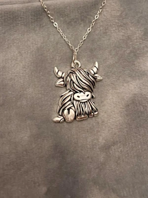 Ko Halsband Highland Cattle Silver imitation  - Så sött halsband med en berlock i form av en ko av rasen Highland Cattle! Berlocken är ca 2 x 2 cm. Halsbandet är justerbart 40-45 cm. 