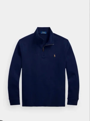 Mörkblå halvzip från Polo Ralph Lauren - Klassisk mörkblå tröja med halv dragkedja från Polo Ralph Lauren. Tröjan har lång ärm, ståkrage och den ikoniska broderade loggan i gult på bröstet. Perfekt för en clean och stilren look.