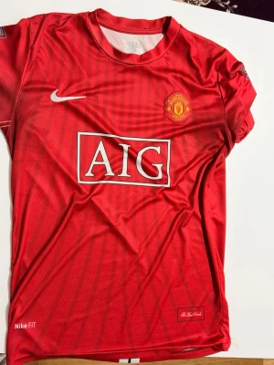 Manchester United Ronaldo tröja - Säljer en röd Manchester United matchtröja från Nike med AIG som sponsor på framsidan och Ronaldo 7 tryckt på ryggen. Tröjan har klubbens emblem på bröstet och är tillverkad i lätt och ventilerande material, perfekt för fotboll eller träning.