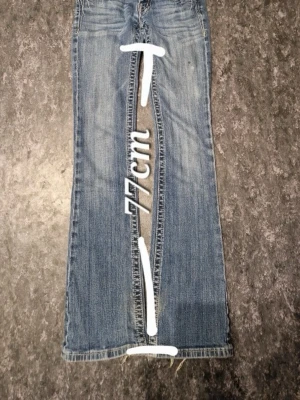 Blå bootcut jeans från Miss Me - Snygga blå bootcut jeans från Miss Me med dekorativa knappar. Klassisk femficksmodell med låg midja och coola detaljer vid linningen. Jeansen är i denim och har måtten 77 cm innerbenslängd och 33 cm midja. Lite slitna baktill längst nere men annars jätte snygga. Priset går att diskutera, dock lägst pris skulle vara 700.