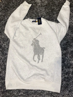 Grå sweatshirt från Polo Ralph Lauren - Sweatshirt från Polo Ralph Lauren med stort grått polospel-tryck på bröstet. Helt ny. S/M. Ej orginal. 260kr färdig prutat o klart!