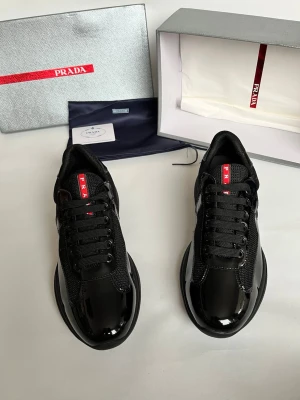 Svarta sneakers från Prada - Snygga svarta sneakers från Prada med blank finish och mesh-detaljer. Skorna har klassisk snörning och en röd logotyp på plösen. Perfekt för dig som vill ha en lyxig och stilren look. Levereras med originalkartong och dustbag.