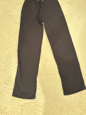 Svarta mjukisbyxor med dragsko - Säljer ett par svarta mjukisbyxor med raka ben och dragsko i midjan. Byxorna har två stora fickor framtill och är gjorda i ett mjukt och bekvämt material, perfekt för chill dagar. Passar dig som gillar en avslappnad stil.