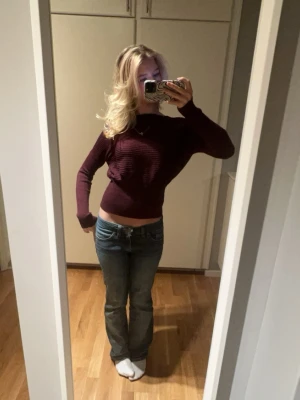 Vinröd ribbstickad tröja - En vinröd ribbstickad tröja med lång ärm och bredare halsringning. Tröjan är kortare i modellen och har en figurnära passform. Materialet är mjukt och stretchigt, perfekt för att skapa en snygg siluett.