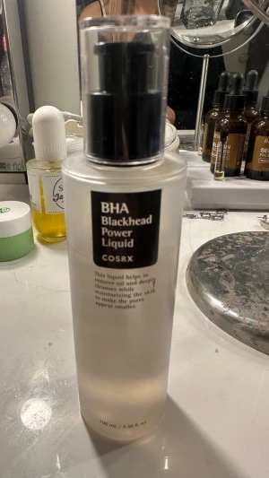 COSRX BHA Blackhead Power Liquid toner - En genomskinlig toner i plastflaska med svart pump från COSRX. Innehåller BHA som hjälper till att ta bort pormaskar och kontrollera överflödig olja samtidigt som huden återfuktas. Flaskan rymmer 100 ml och har en stilren, minimalistisk design.
