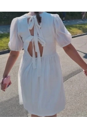 Vit kortklänning med puffärm och knyt - Söt vit kortklänning med puffärmar och öppen rygg med dubbla knytband. Klänningen har en luftig passform och är gjord i ett lätt, strukturerat bomullstyg. Perfekt för varma dagar och ger en romantisk vibe.
