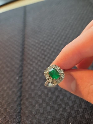 Silverring med grön sten och kristaller - Snygg silverfärgad ring med en stor, fyrkantig grön sten i mitten och gnistrande klara kristaller runt om. Jag har ganska stora händer och på mig passar den inte.