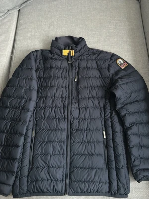 Marinblå lightweight jacka från Parajumpers - Snygg marinblå lightweight jacka  från Parajumpers med klassisk design och hög krage. Jackan har tre dragkedjeförsedda fickor framtill och en ikonisk patch på ärmen. Superlätt material som håller dig varm utan att kännas tung. Perfekt för våren.