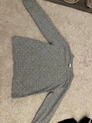 Grå stickad tröja med pärlor från Zara - Supersnygg grå stickad tröja från Zara med små pärlor över hela framsidan. Tröjan har lång ärm och en klassisk rund halsringning. Perfekt att styla med jeans eller kjol för en trendig look.