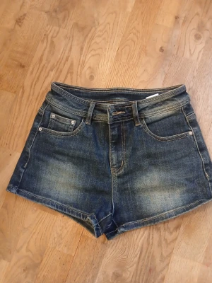 Mörkblå denimshorts med fickor stl xs - Snygga mörkblå jeansshorts i klassisk femficksmodell med bälteshällor och knappstängning. Shortsen har slitna detaljer och bakfickor med lock och knapp. Perfekta till sommaren för en avslappnad look. Står s men skulle verkligen säga xs dem är även lite mindre vid midjan