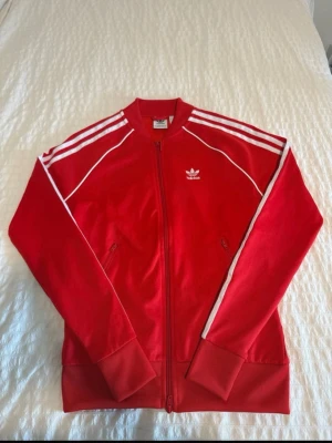 Röd Adidas ziptröja med vita ränder - Säljer en röd ziptröja från Adidas. helt ny aldrig andvänt