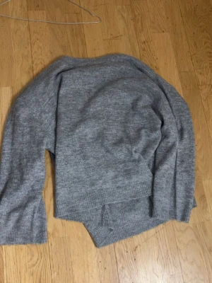 Grå stickad tröja i ullmix - Mysig grå stickad tröja med avslappnad passform och långa ärmar. Tröjan har ribbstickade muddar vid ärmslut och nederkant, perfekt för kyliga dagar. Materialet känns mjukt och värmande, troligen en ullblandning.