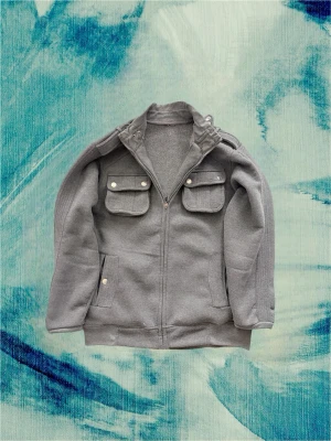 Grå zip-up jacka med fickor - Säljer den coola och unika ulljacka i stl M. Passar dig som normalt bär M. Den påminner om en blandning av en skepparkavaj och en jacka med zip. Hör av dig vid frågor! OBS: Den har lite fläckar här o där som troligtvis går bort i tvätten.