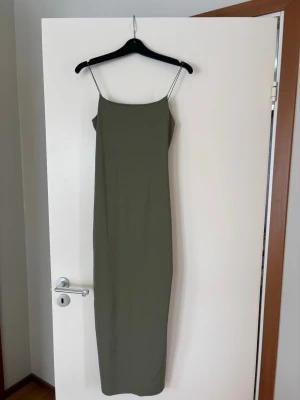 Olivgrön långklänning med tunna band - Säljer en stilren olivgrön långklänning med tunna axelband och rak passform. Klänningen har minimalistisk design utan synliga detaljer och är tillverkad i ett mjukt, stretchigt material som ger en bekväm känsla. Använd 1 gång, köpt på Pull&Bear i storlek S 💚